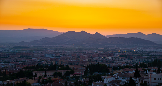 A beautiful orange sunset over a mountain range and town in Granada, Spain