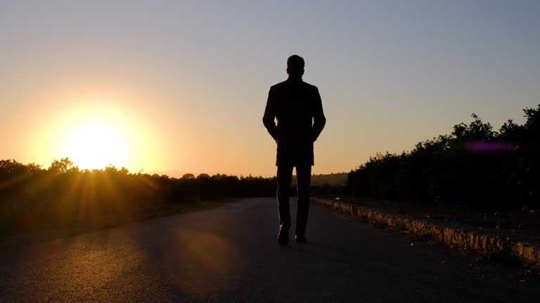 Silhouette of a man is walking on a road at golden sunset.