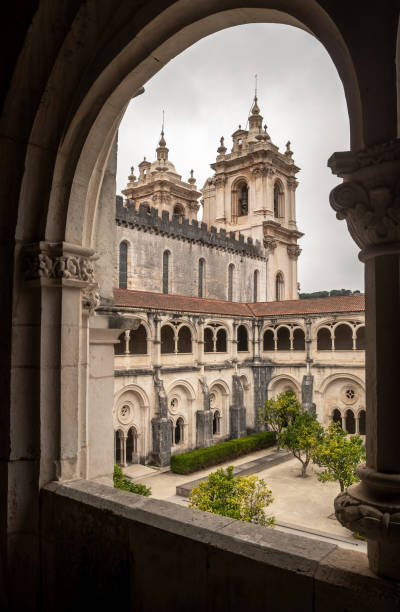 View of the cloister of D. Dinis and the bell towers framed by the cloister archway, at the Monastery of Alcobaça in Portugal. Alcobaça, Portugal - August 24, 2022: View from the first floor of the cloister, through one of the arcades, over the garden and two wings of the cloister. In the background we have two bell towers that are the towers of the main facade of the monastery.
The cloister of D. Dinis is also known for the cloister of silence, a name due to the prohibition of conversation at that time in that place.
The cloister was built between 1308 and 1311. The cloister has a perimeter of about 203 meters. alcobaca photos stock pictures, royalty-free photos & images