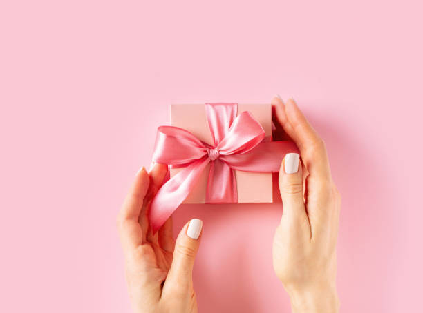 istock Womans hands holding wrappes gift box with ribbon on pink background 1463537267