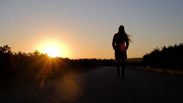 Silhouette of a woman is walking on a road at golden sunset.
