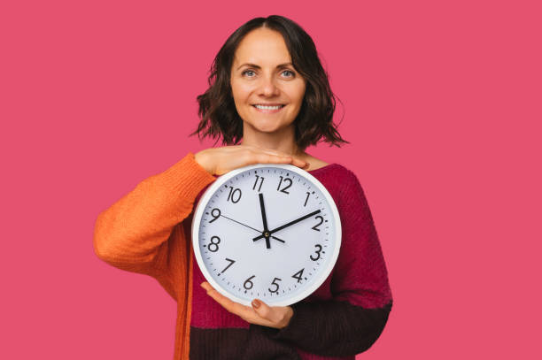 istock It is time says a smiling woman while holding a big white round clock. 1463539809