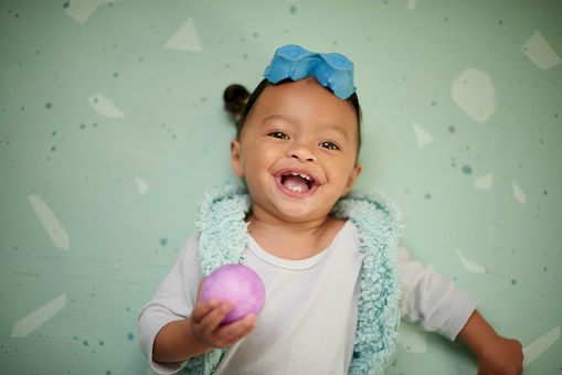 Baby, girl and studio portrait with ball, lying and smile for childhood happiness, growth or development. African infant child, happy female or toys in hand for learning, laughing and excited face