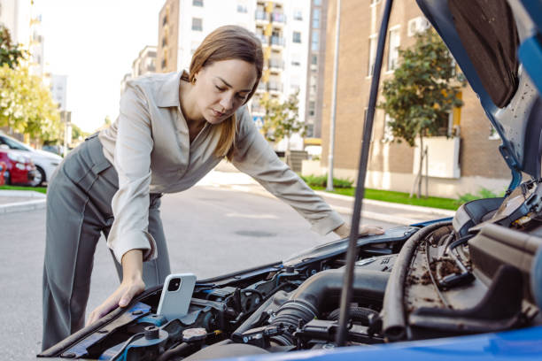 istock Woman standing next to her car trying to fix it while watching online instructions 1463544020