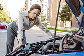 Woman standing next to her car trying to fix it while watching online instructions