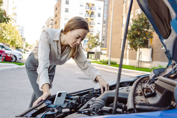 istock Woman standing next to her car trying to fix it while watching online instructions 1463544105