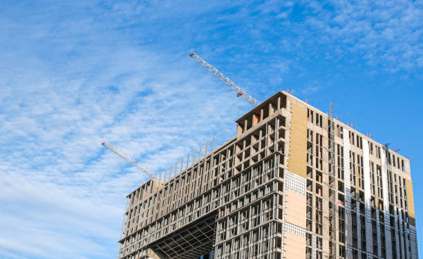 cantiere. gru edili e un edificio in costruzione su uno sfondo blu del cielo. le gru edili stanno lavorando, i muri degli edifici vengono eretti. - high rise apartments foto e immagini stock