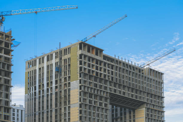 cantiere. gru edili e un edificio in costruzione su uno sfondo blu del cielo. le gru edili stanno lavorando, i muri degli edifici vengono eretti. - high rise apartments foto e immagini stock