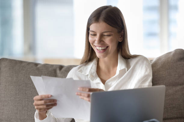 istock Cheerful young freelance employee woman reading document at laptop 1463546268