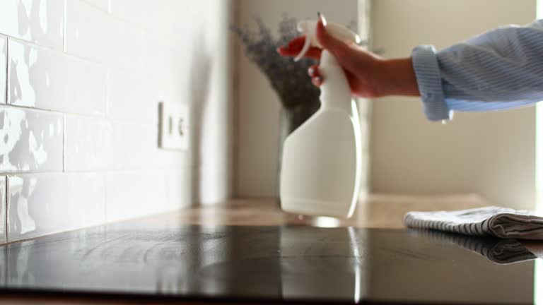 Cleaning induction electric stove at kitchen countertop. close up housewife's hands cleans kitchen induction hob with cleaning spray. Woman cleaning house, cleaning service. Housekeeper disinfecting.