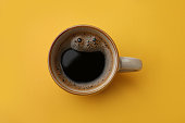 Cup of delicious black coffee on yellow background, top view