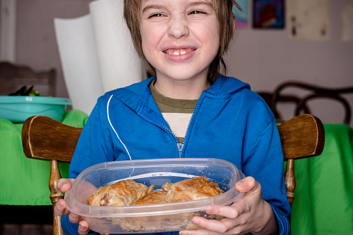 A young boy is holding some leftover chicken in a reusable plastic container