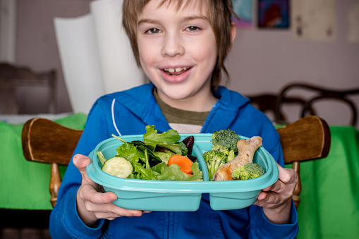 A boy is eating a salad with in a reusable plastic container