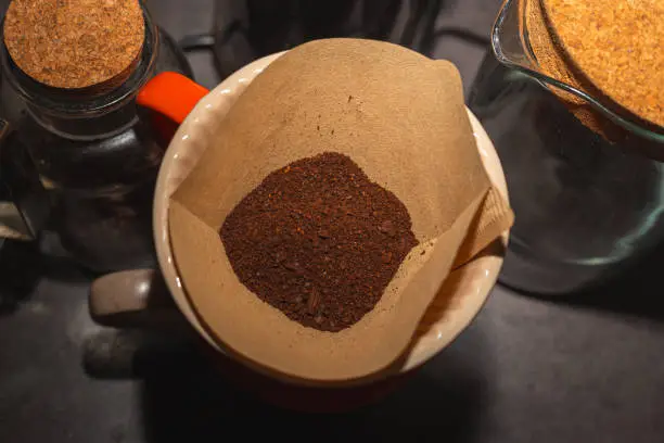 Photo of Brewing coffee in a funnel. The process of making branded coffee in a funnel on a gray wooden table. In the early morning, pour the coffee that blooms in the dropper.