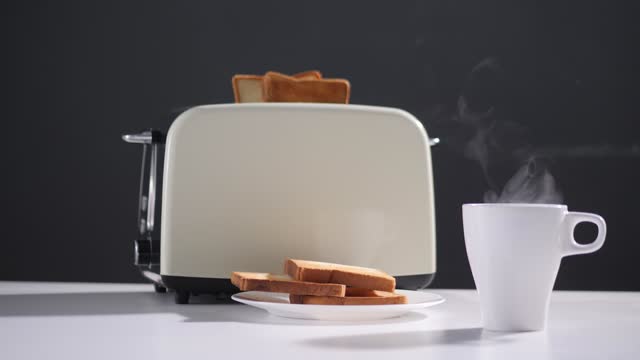 White cup of hot beverage, coffee or tea with steam. Toaster with ready fried toast inside and on plate. Healthy brecfast. Selective focus.