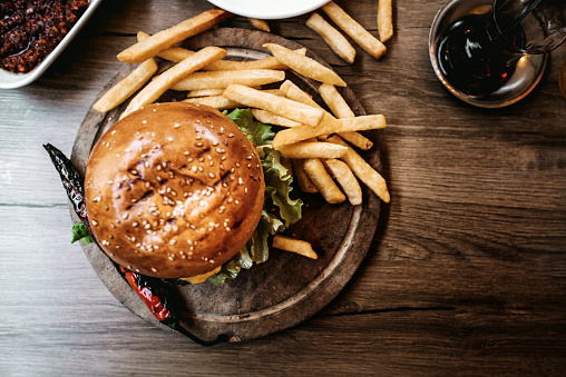 Top view of Delicious double burger with french fries and vegetables on wooden cutting board