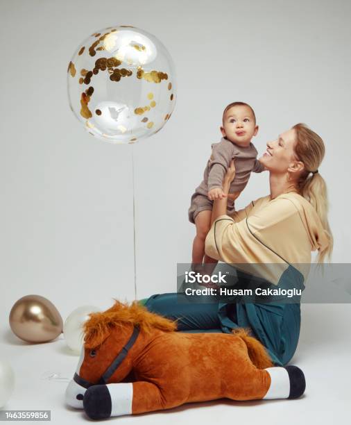 Baby Boy In Mothers Lap Looking At Her Flying Balloon In Front Of White Background Stock Photo - Download Image Now