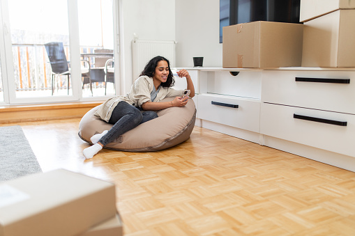 Woman Using Her Smartphone On A Beanbag In Her New Apartment