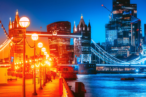 Panoramic view of The City of London cityscape skyline with Tower Bridge, Thames path metropole financial district modern skyscrapers after sunset on the night with illuminated buildings with Thames river and cloudy sky in London, UK