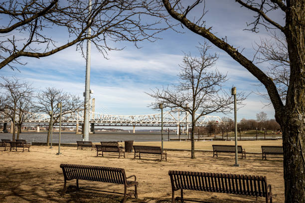 Rows of empty benches facing bridges of Kentucky river in Louisville waterfront park during mid winter.
