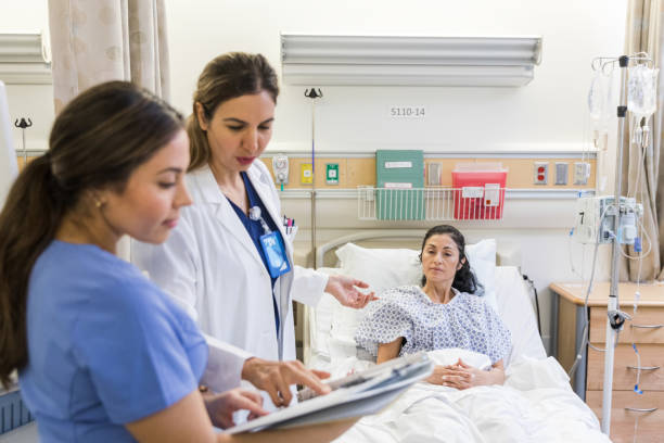 While talking to patient, doctor checks medical test results The mature adult female doctor stops to check the results of the medical tests as she is talking to the mature adult female patient. sick woman hospital bed stock pictures, royalty-free photos & images