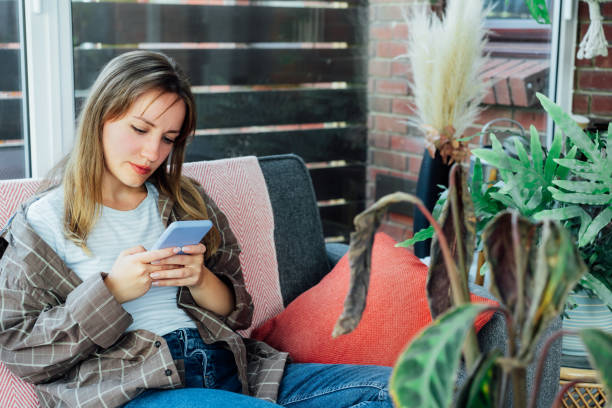 istock Young woman using mobile phone for searching info about houseplants disorders, it's identification and treatment for dried, sunburn leaf of potted plant Calathea. Houseplants diseases. Home gardening 1463568348