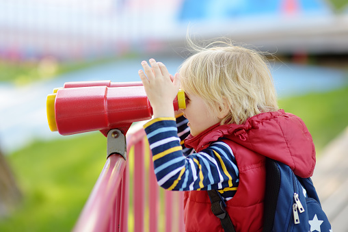 Little boy playing with binoculars. Child is having fun while walking on playground of kindergarten. Outdoor activities and entertainment for children. Modern equipment for kids street playgrounds.