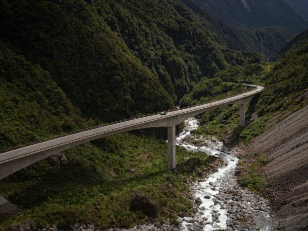 автомобили едут по бетонному мосту otira viaduct через зеленую альпийскую долину реки на перевале артурс южные альпы новая зеландия - arthurs pass national park стоковые фото и изображения