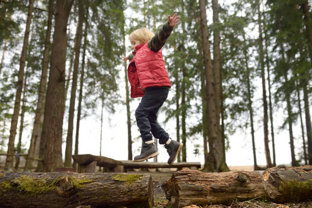 un ragazzino in gilet rosso sta giocando a fare il ramo e si diverte nella foresta all'inizio della primavera. attività per bambini. attività ricreative all'aperto per famiglie - children only tree area exploration freshness foto e immagini stock