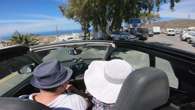Happy couple driving on country road iin classic convertible sports car, Santorini Island, Greece
