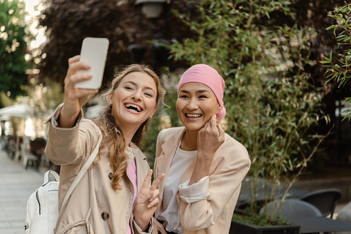 Portrait of an Asian female cancer patient with a headscarf and her best friend enjoying in the city and taking a selfie