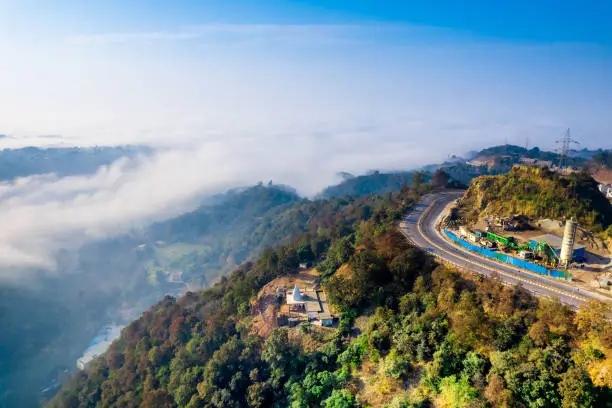 aerial drone pan shot from mountain hill road highway with cars moving on it to valley filled with fog clouds stretching into distance showing himalayas of himachal pradesh India