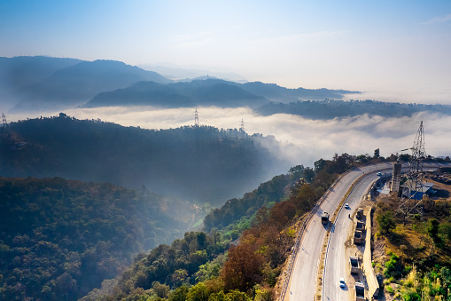 aerial drone pan shot from mountain hill road highway with cars moving on it to valley filled with fog clouds stretching into distance showing himalayas of himachal pradesh