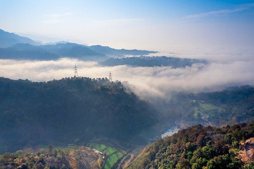 aerial drone shot of valley with clouds stretching into distance showing himalayas of himachal pradesh India with electrical power lines and towers mounted on the peaks
