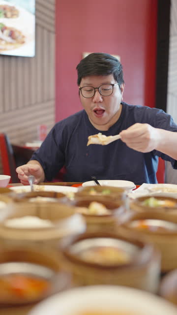 Large build Asian man eating on a table full of dim sum in Chinese restaurant