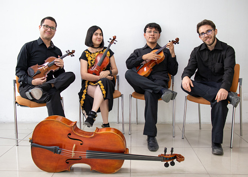three men and a girl mixed group of musicians with wooden string instruments, sitting against a white wall