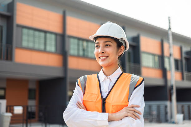 istock Confident engineer woman standing at modern home building construction. Architect with white safety helmet at construction site. Mechanic service factory Professional work job occupation in uniform. 1463615655