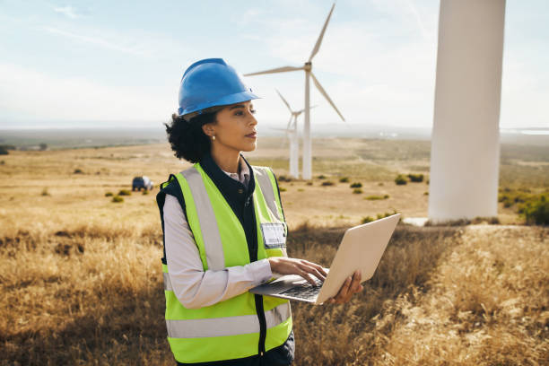 windmill on farm, black woman in clean energy typing on laptop and electricity generation with wind turbines in africa. renewable power, female engineer in agriculture environment and safety gear - wind turbine fuel and power generation clean industry imagens e fotografias de stock