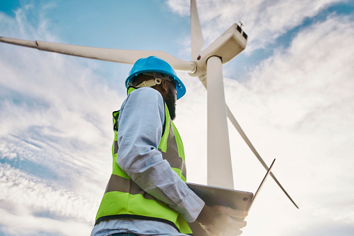 Wind turbine, engineer man and laptop with sky for renewable energy, power and electricity. Electrician or technician person for farm windmill, eco and green environment inspection and maintenance