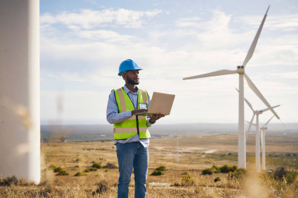 engineer man, windmill and laptop on farm for renewable energy, power and electricity outdoor. electrician or technician in nature for wind turbine, eco and green environment sustainable maintenance - power line electricity construction fuel and power generation imagens e fotografias de stock