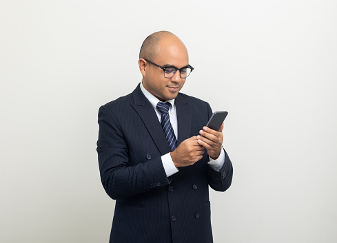Portrait of Young asian businessman using cell phone on isolated white background. Handsome middle aged Indian businessman holding smartphone in office uniform.