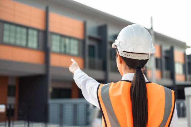 istock Confident engineer woman standing at modern home building construction. Architect with white safety helmet at construction site. Mechanic service factory Professional work job occupation in uniform. 1463616176