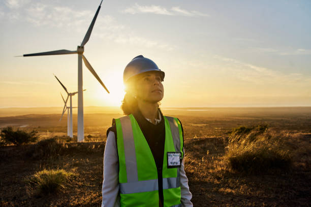 Renewable energy, windmill and engineer woman on farm for sustainability, power and electricity. Technician person in nature for wind turbine and green environment innovation maintenance at sunset stock photo