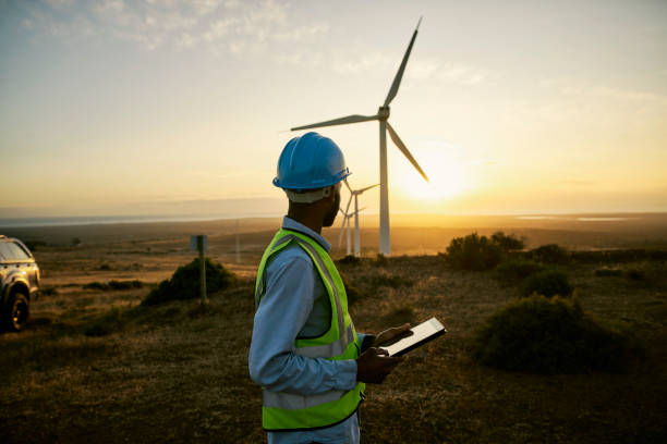 Engineer man, tablet and wind turbine on sunset farm for clean energy, power and electricity. Electrician or technician person in nature for windmill, eco and green environment innovation maintenance stock photo