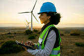 Engineer woman, tablet and windmill for renewable energy, power and electricity innovation. Electrician or technician person in sunset nature for wind turbine and eco environment future maintenace