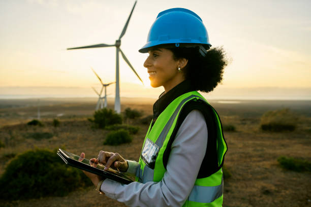 Engineer woman, tablet and windmill for renewable energy, power and electricity innovation. Electrician or technician person in sunset nature for wind turbine and eco environment future maintenace stock photo