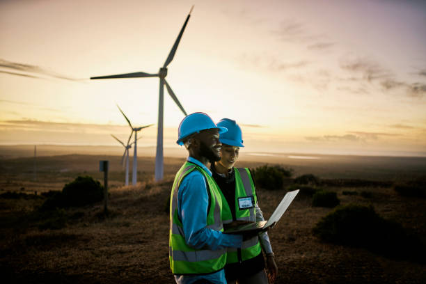 Laptop, farm and engineer team together at night for renewable energy, power and wind turbine. Electrician or technician man and woman in nature for electricity, eco and green environment maintenance stock photo