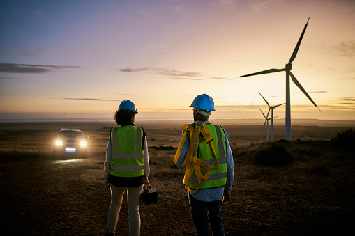 Wind turbine, farm and maintenance engineer team at night for renewable energy, power and electricity. Electrician or technician man and woman at windmill field for eco or green environment innovation