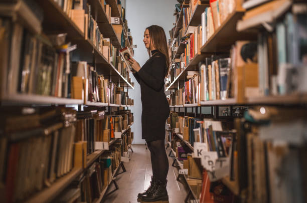 istock Female librarian is reading a book while standing among the bookshelves 1463629902