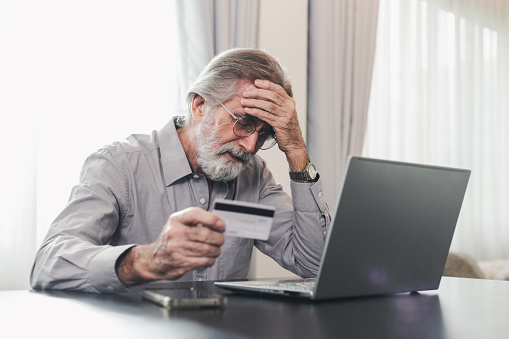 Anciano molesto que sostiene una tarjeta de crédito por computadora portátil que tiene problemas para preocuparse por los datos de seguridad financiera o la seguridad de los pagos en línea. Cliente bancario preocupado por problema con tarjeta de crédit photo